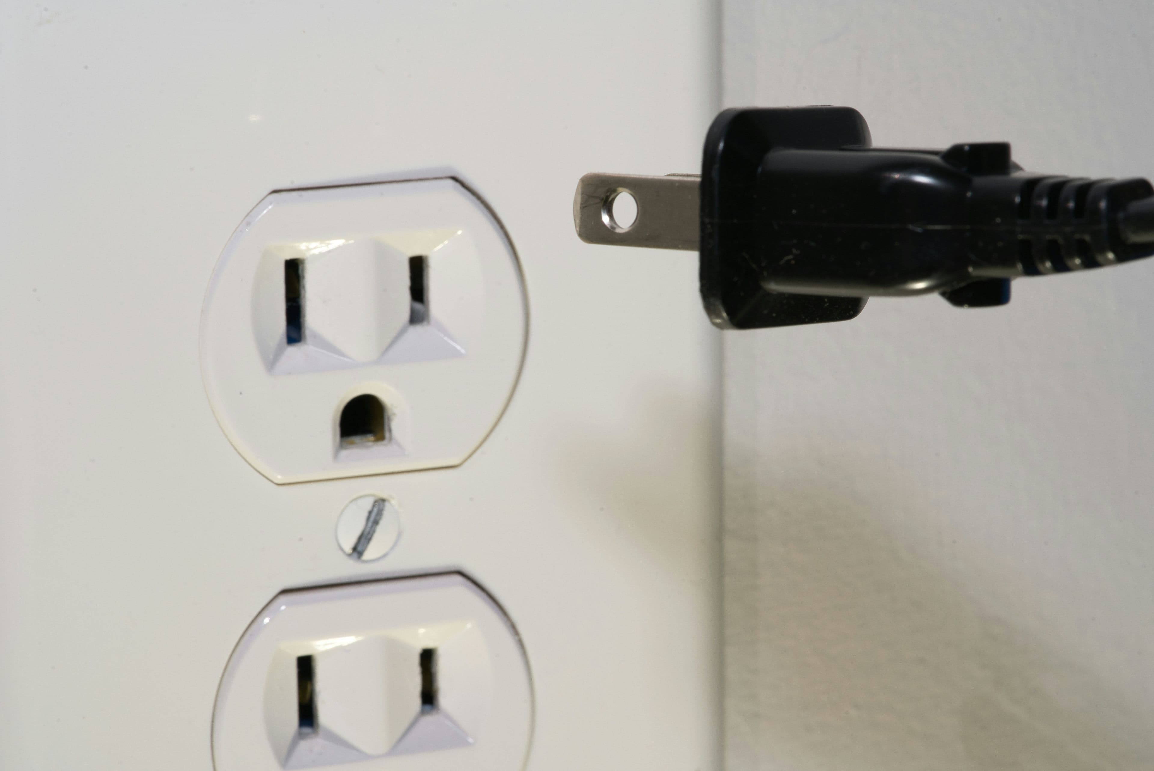 A white smart plug connected to a wall socket with a phone showing its app